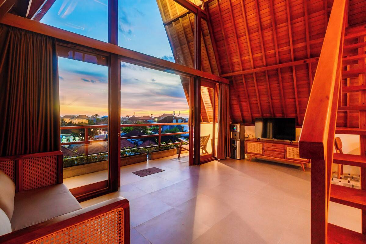 A spacious living area with large windows, a wooden ceiling, and a view of the cityscape.