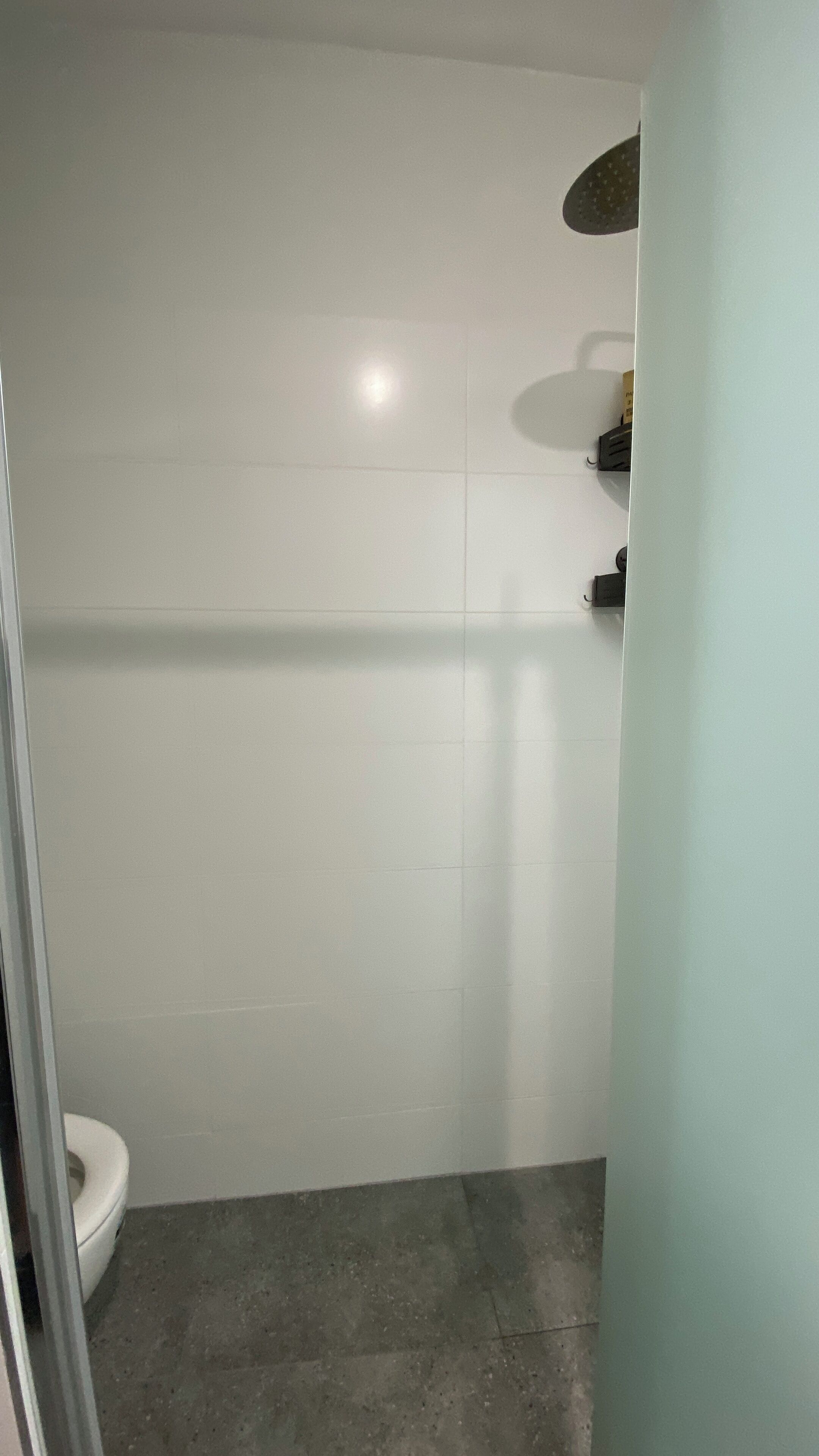 Une salle de bain avec des carreaux blancs, des toilettes et un espace douche.