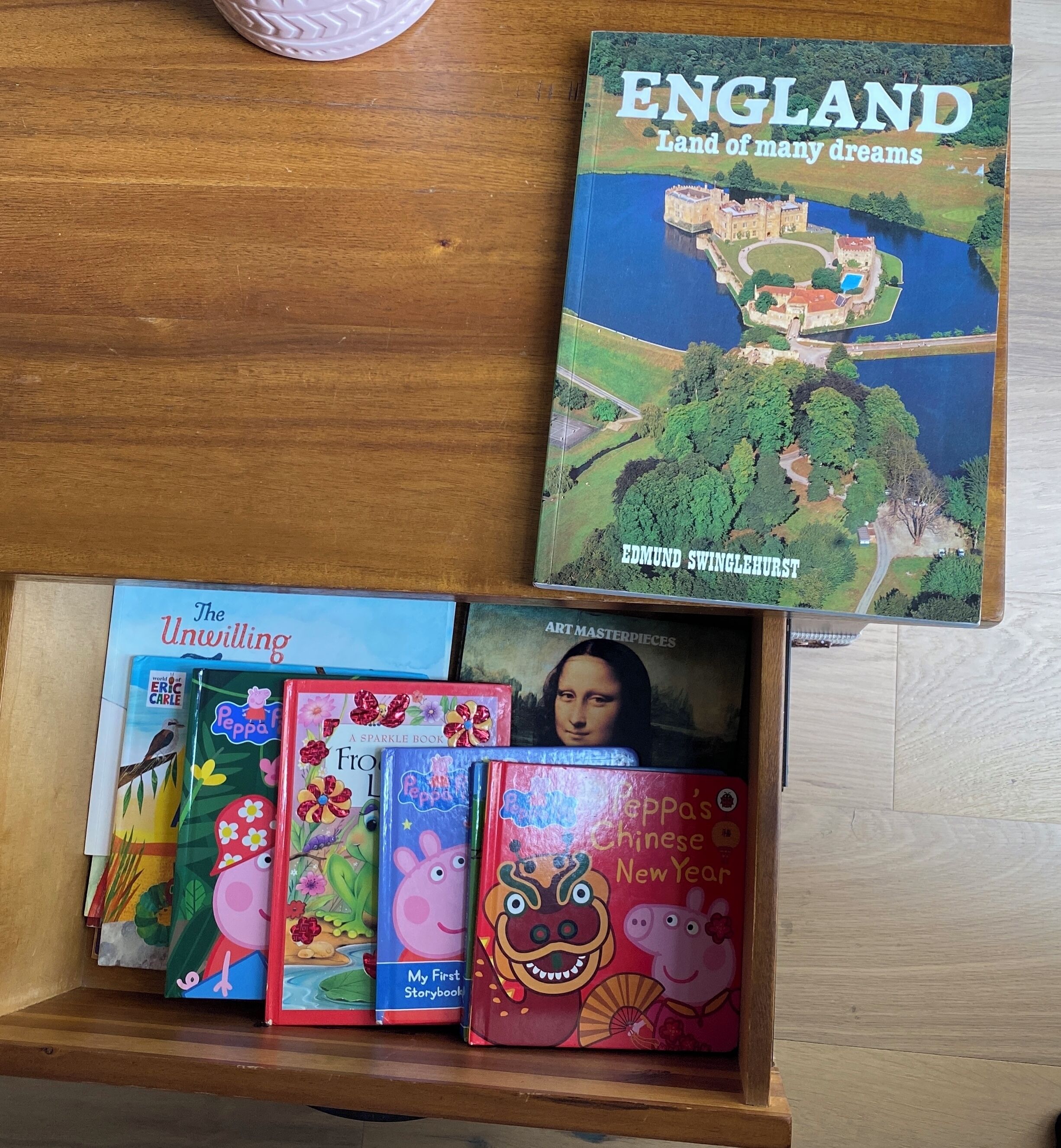 A wooden table with a book titled 'ENGLAND Land of many dreams' and a drawer containing children's books.