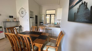 A dining area with a wooden table and chairs, a kitchen in the background, and a painting on the wall. - 2 bed apartment for up to 6 people in awesome beachside Hampton (Hampton)