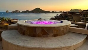A hot tub with a stone exterior, overlooking a coastal view with buildings and mountains in the background.