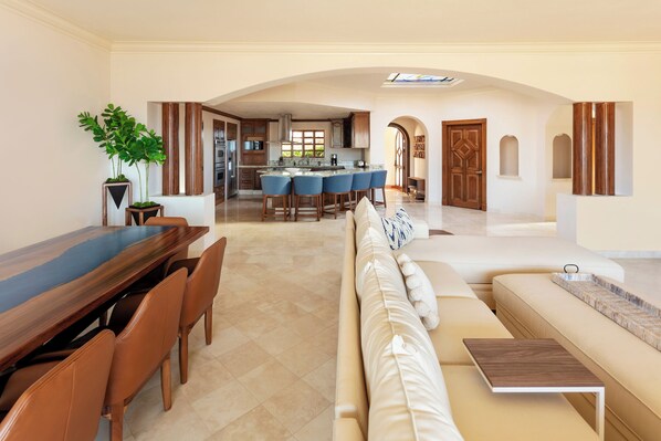 A spacious living area with a dining table, a sofa, and a kitchen in the background.