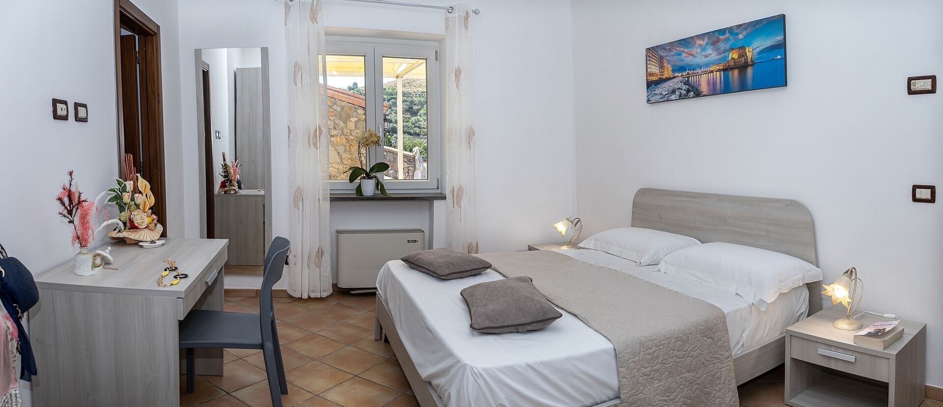 Une chambre à coucher avec un lit, des tables de chevet, un bureau et une fenêtre avec des rideaux.