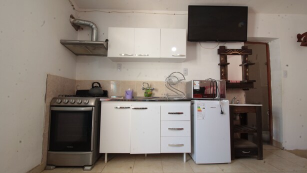 A compact kitchen with a gas stove, a microwave, a small refrigerator, white cabinets, a sink, and a television mounted above the cabinets. - Monoambiente Centrico en Tilcara (Tilcara)