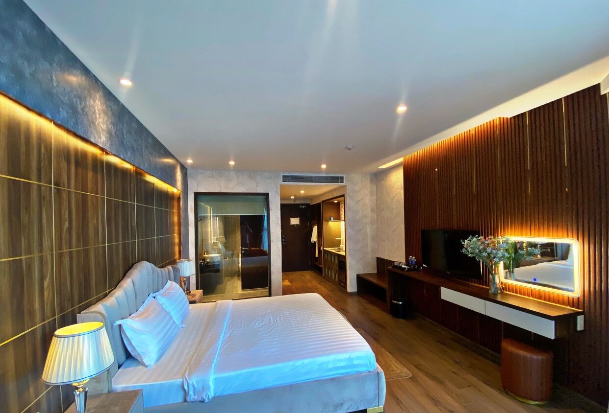 A modern hotel room with a large bed, a TV, a vanity, and a mirror.