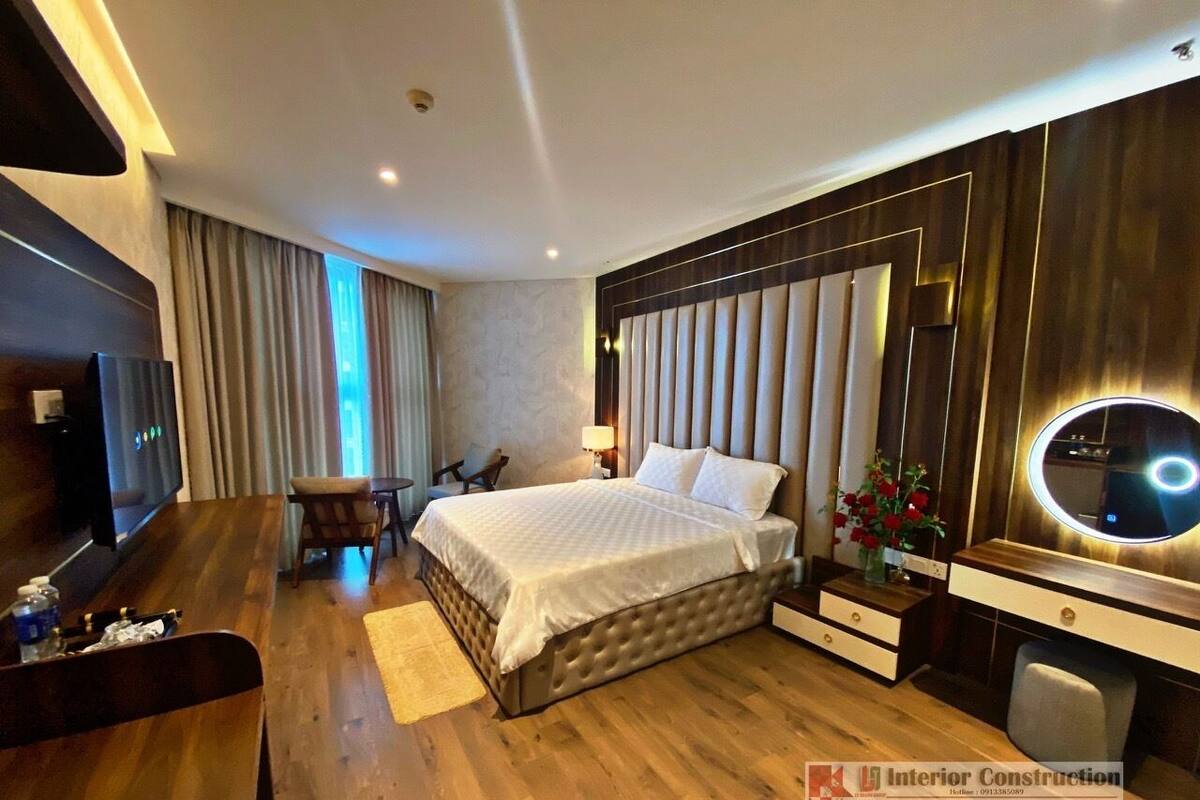 Ein modernes Hotelzimmer mit einem großen Bett, einem Schreibtisch, einem Sessel, einem Fernseher und einem Schminktisch mit Spiegel.