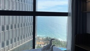 Ein Hotelzimmer mit großem Fenster und Blick auf das Meer und die Stadt.