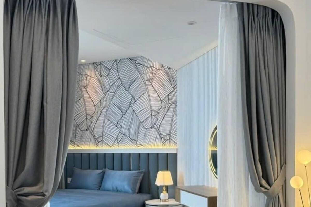 Ein modernes Schlafzimmer mit Bett, Nachttisch, Lampe und Blick auf die Stadt durch ein Fenster.