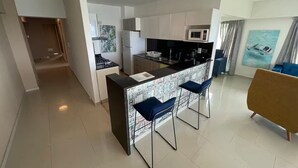 A modern kitchen with a central island, bar stools, a microwave, and a refrigerator.