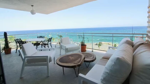 A balcony with white furniture, a wooden table, and potted plants.