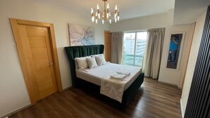 A bedroom with a large bed, a chandelier, a window with curtains, and a door.
