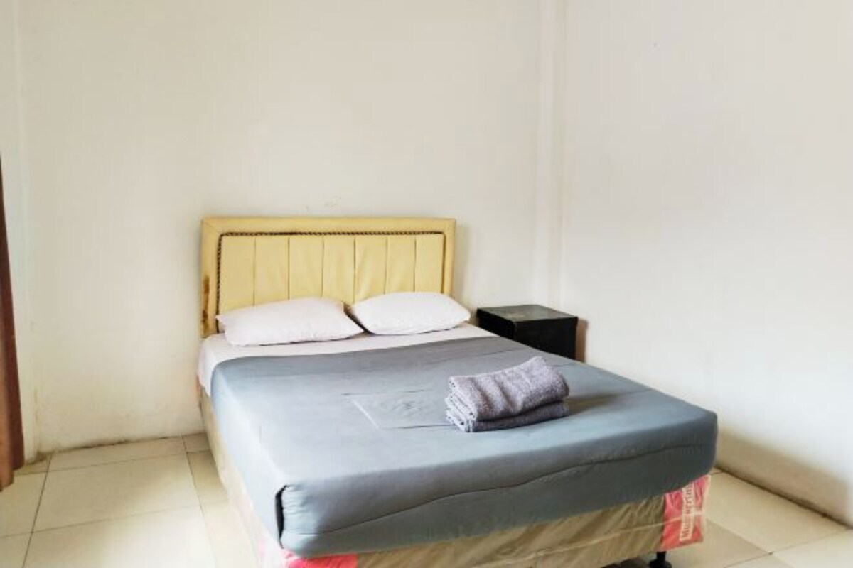 Una cama individual con cabecera, dos almohadas, una mesita de noche y una colcha.