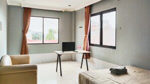 Una habitación de hotel con una cama, un escritorio con computadora y dos ventanas con cortinas.