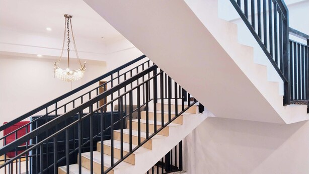 Una escalera con barandillas negras y escalones blancos que conduce a un piso superior.