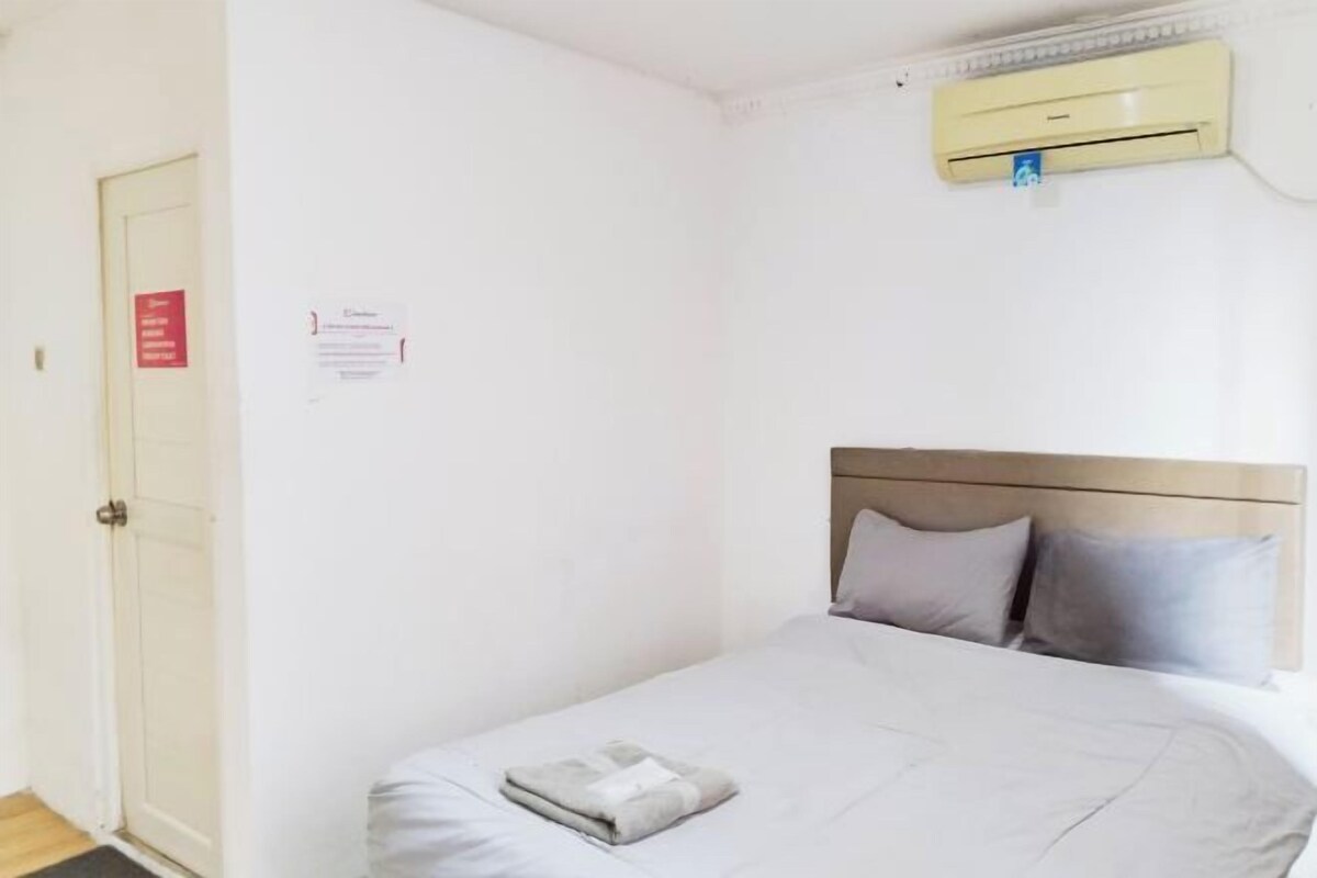 A single bed with a headboard, a wall-mounted air conditioner, and a door with a sign.