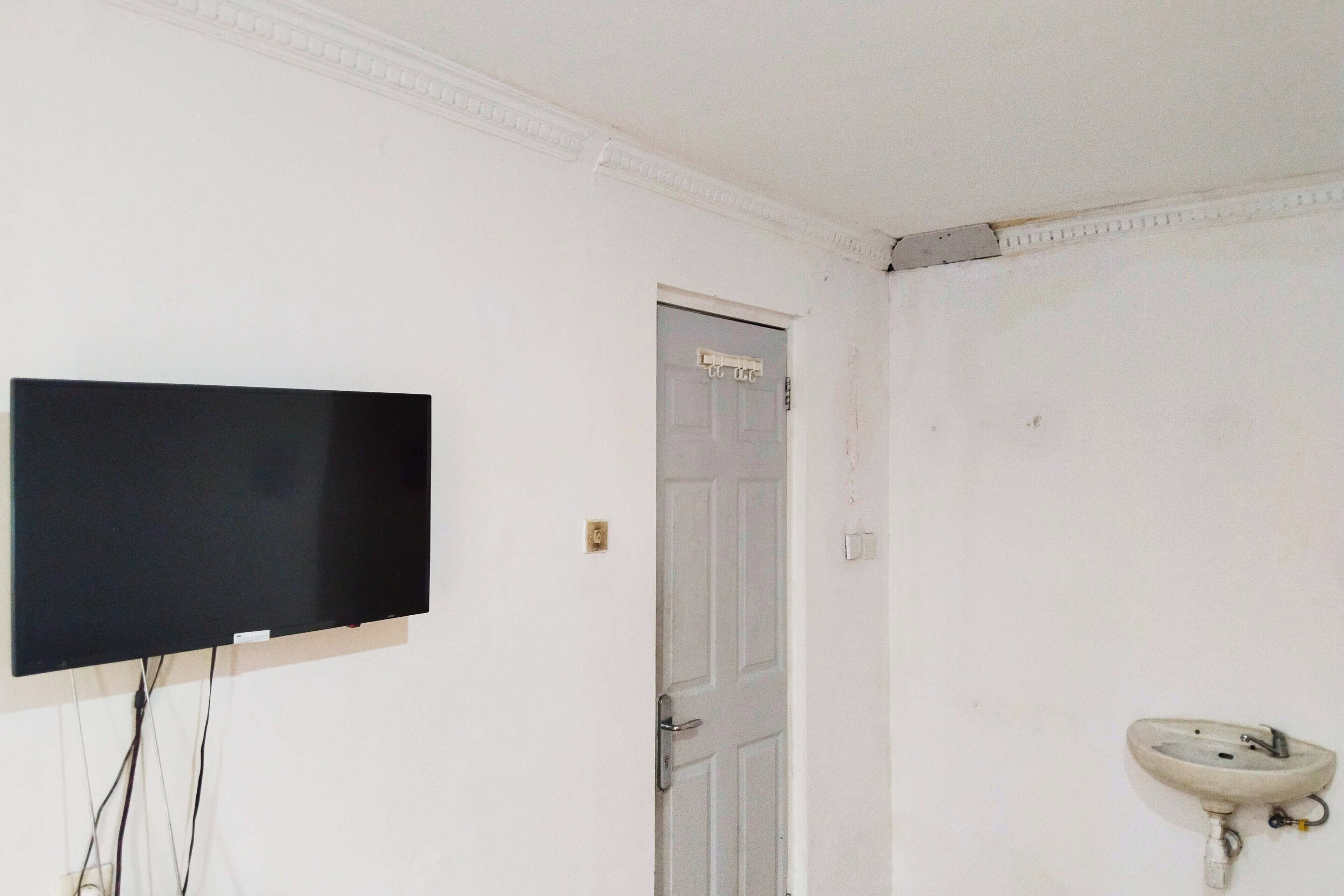 Una habitación con televisión montada, una puerta y un lavamanos fijado a la pared.