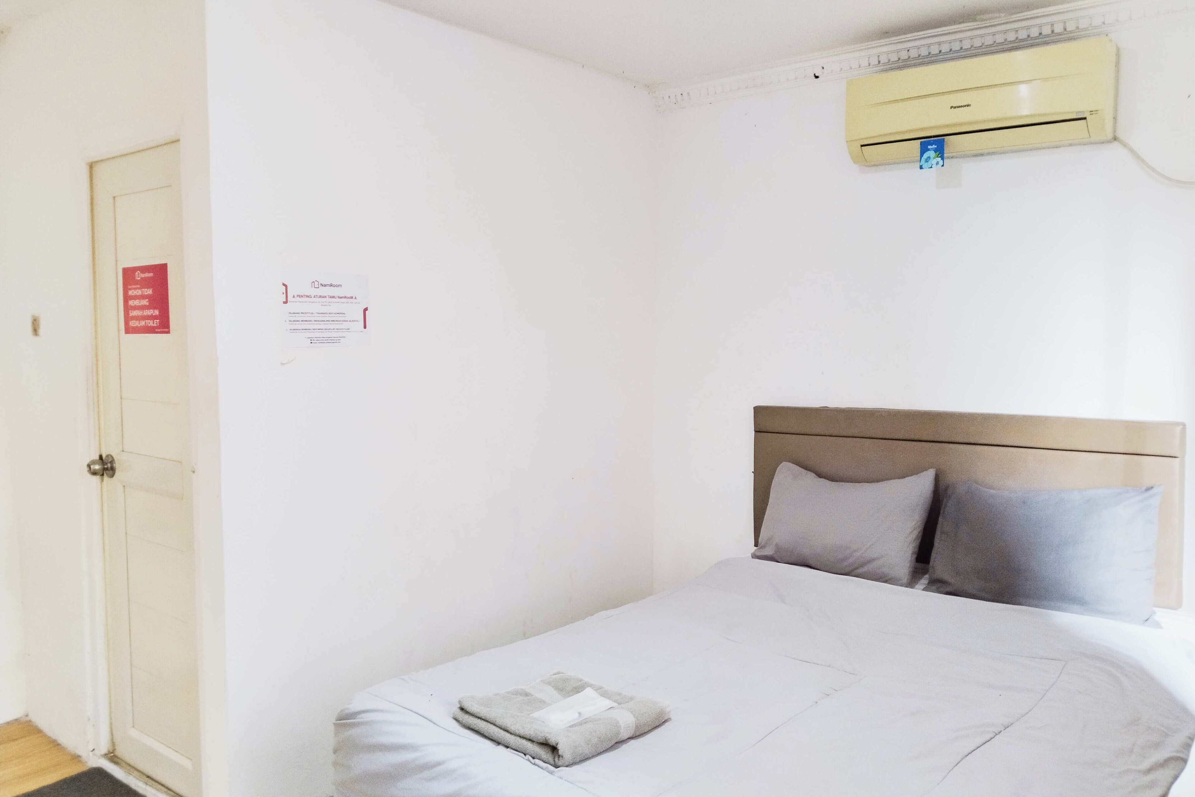 Ein Einzelbett mit Kopfstütze, ein gefaltetes Handtuch und eine Wand-Klimaanlage.