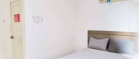 Ein Einzelbett mit Kopfstütze, ein gefaltetes Handtuch und eine Wand-Klimaanlage.
