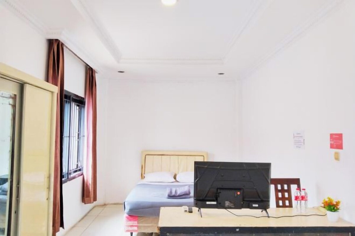 Une pièce comprenant un lit, un bureau avec un ordinateur, une fenêtre avec des rideaux et une porte.