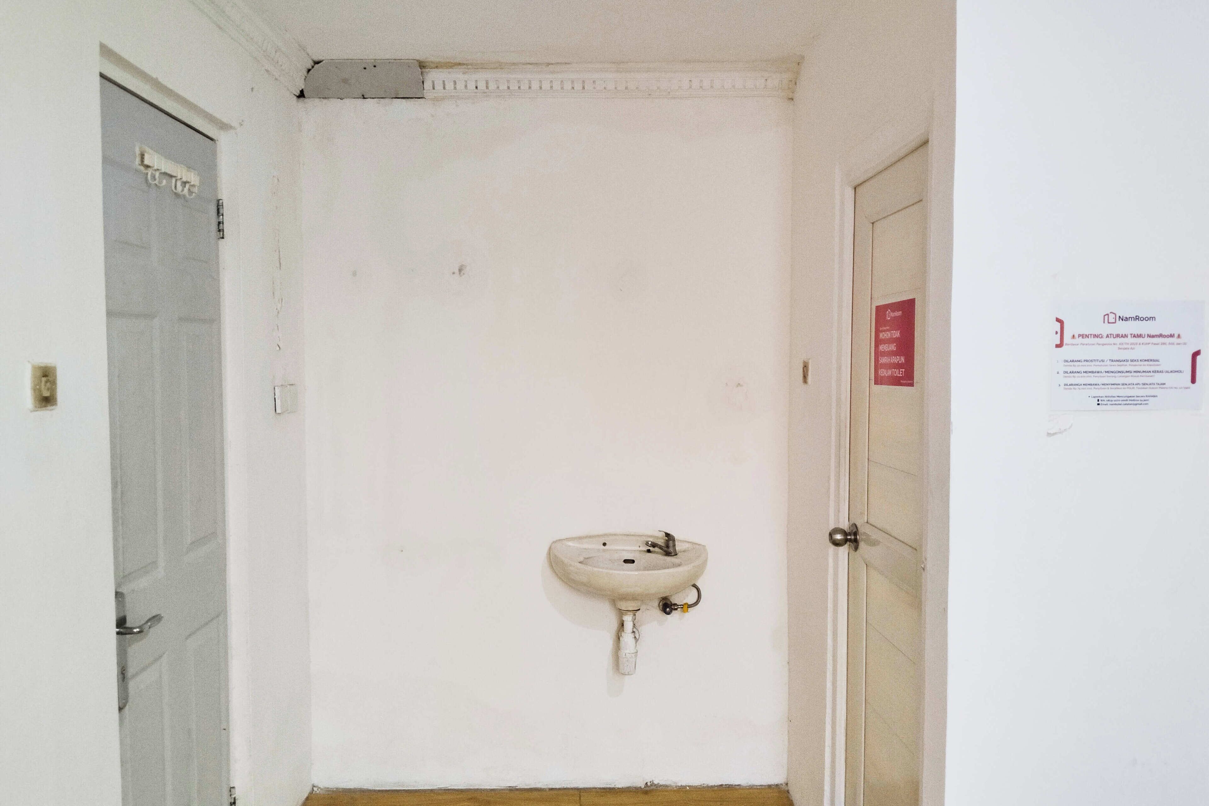 A narrow hallway with a white wall, a door on the left, and a sink mounted on the right wall.