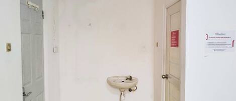 A narrow hallway with a white wall, a door on the left, and a sink mounted on the right wall.