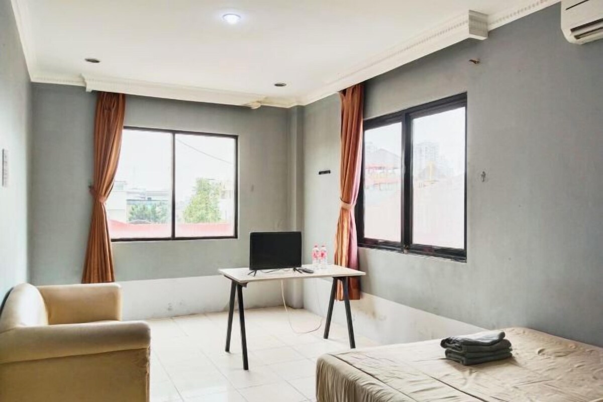 A room with a bed, a desk, a chair, and two windows with curtains.