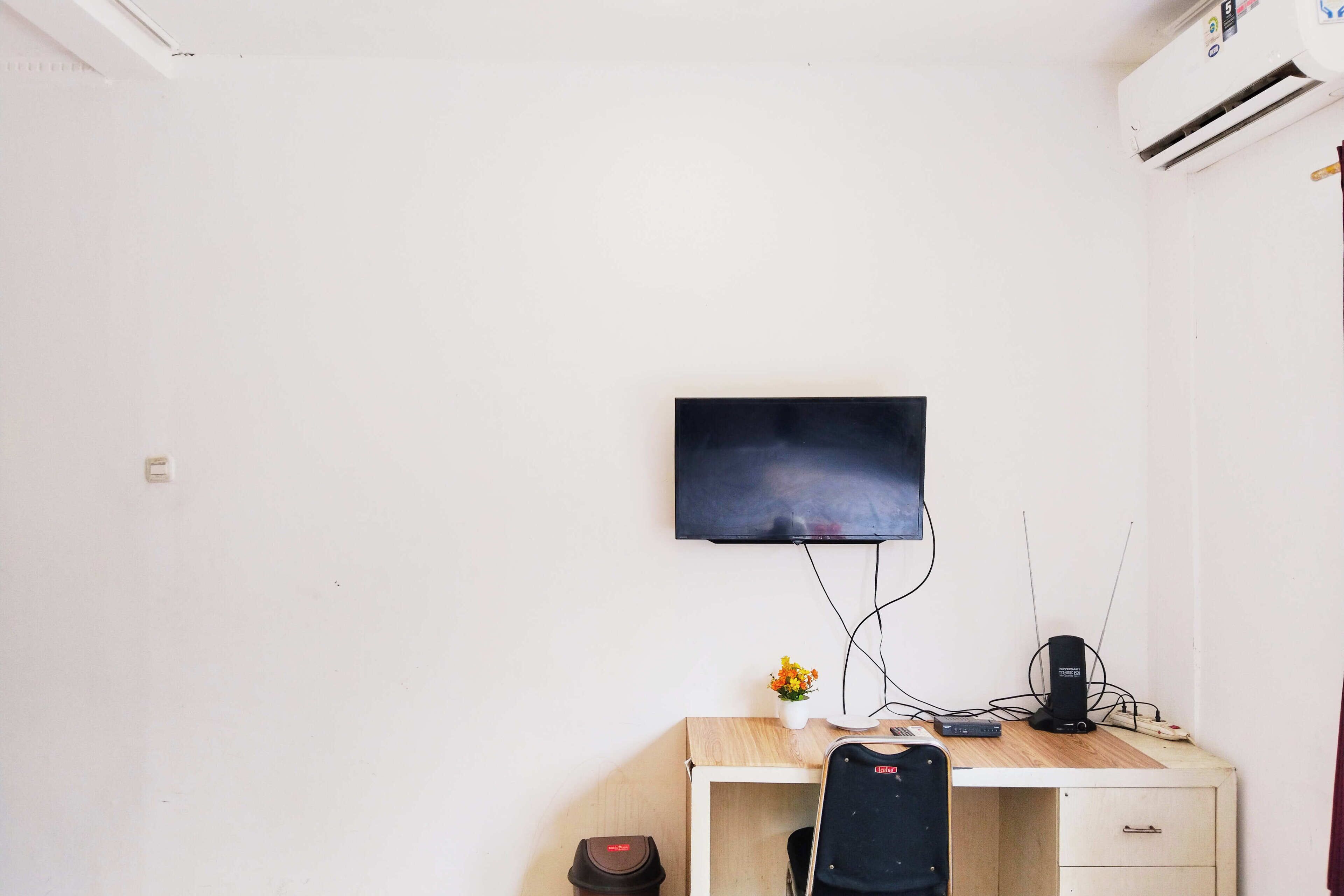 Ein Zimmer mit Schreibtisch, Stuhl, Wandfernseher und Klimaanlage.