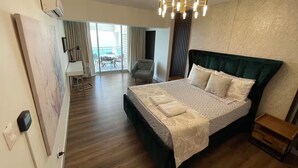 A spacious bedroom with a large bed, a chandelier, a desk, and a view of the outdoors.