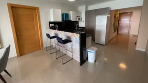 A modern kitchen with a central island, bar stools, a microwave, and a refrigerator.