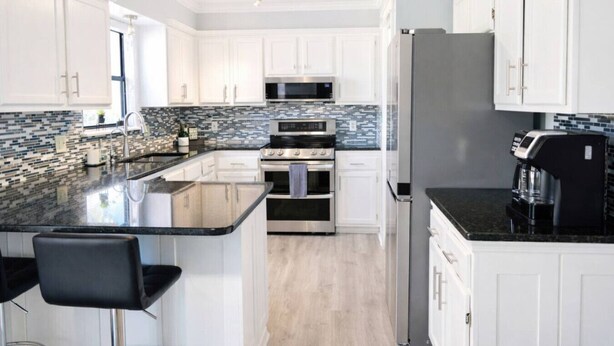A modern kitchen with white cabinets, a black countertop, and a stainless steel refrigerator.