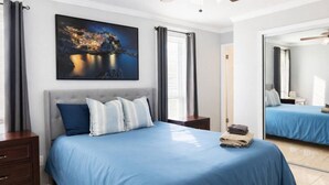 A bedroom with a bed, a nightstand, a mirror, and a painting.