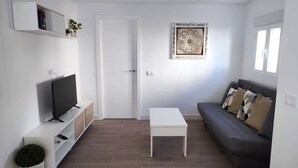Un salon moderne avec un téléviseur à écran plat, une table basse blanche, un canapé gris et un élément décoratif mural.
