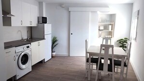 Une cuisine compacte équipée d’un lave-linge, d’un four à micro-ondes et d’un coin repas avec une table et des chaises.