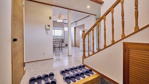 A staircase with wooden balusters and a landing area with multiple pairs of shoes. - Fuji Holiday (Fujiyoshida)
