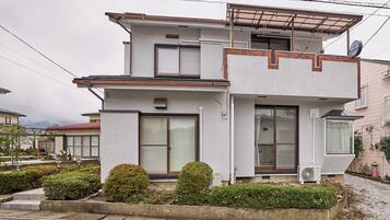 A two-story residential building with a flat roof, large windows, and a small balcony.