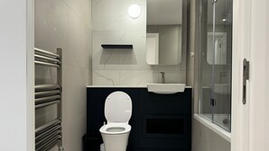 A modern bathroom with a toilet, sink, and glass shower enclosure. - Excel London Gateway Apartments (London)