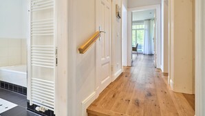 Un pasillo con piso de madera, paredes blancas y una puerta con perchero.
