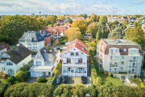 A residential area with a prominent white house featuring a red roof, surrounded by other houses and lush greenery.