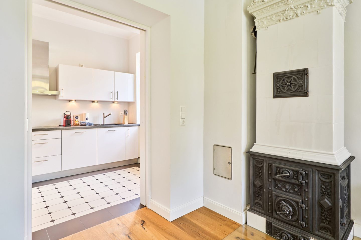 A modern kitchen with white cabinets, a black and white tiled floor, and a dark wooden cabinet with intricate carvings.