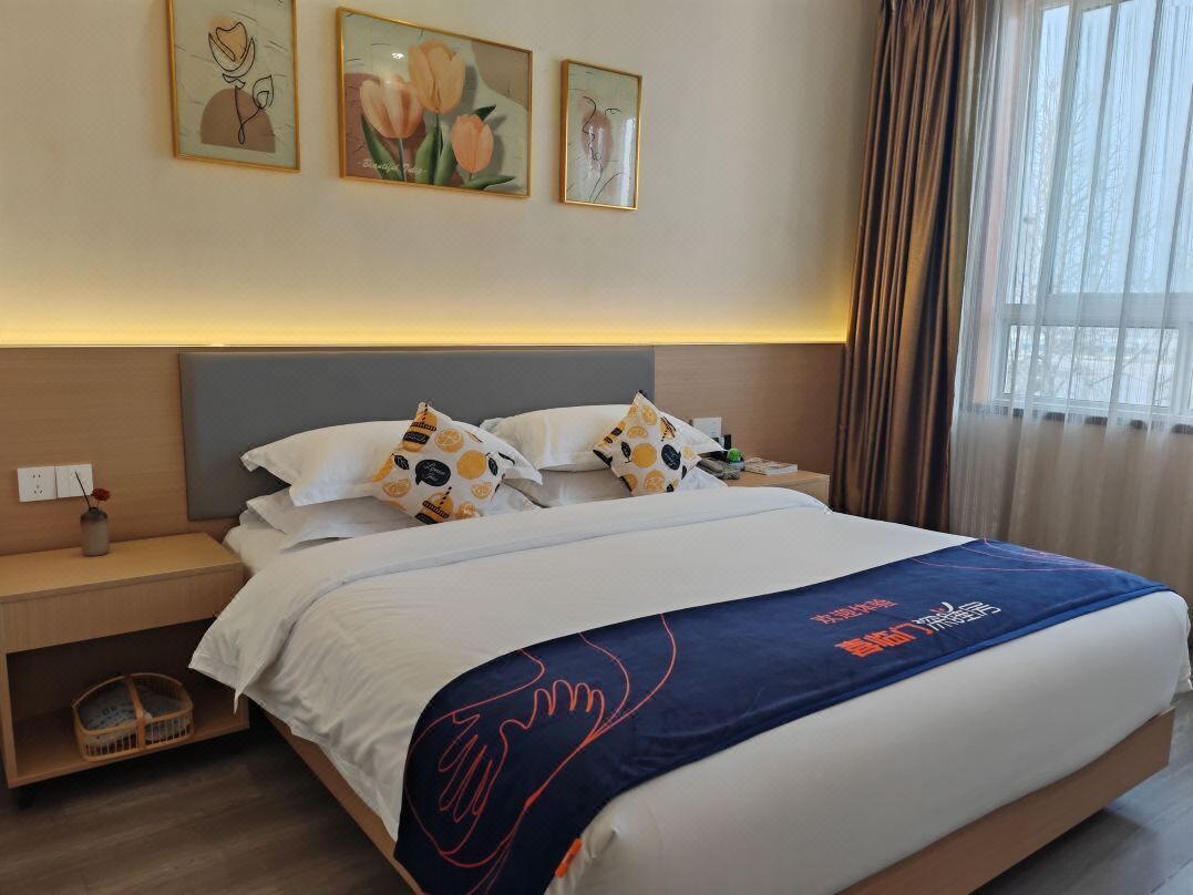 Quarto de hotel com cama, mesa de cabeceira, abajur e janela com cortinas.
