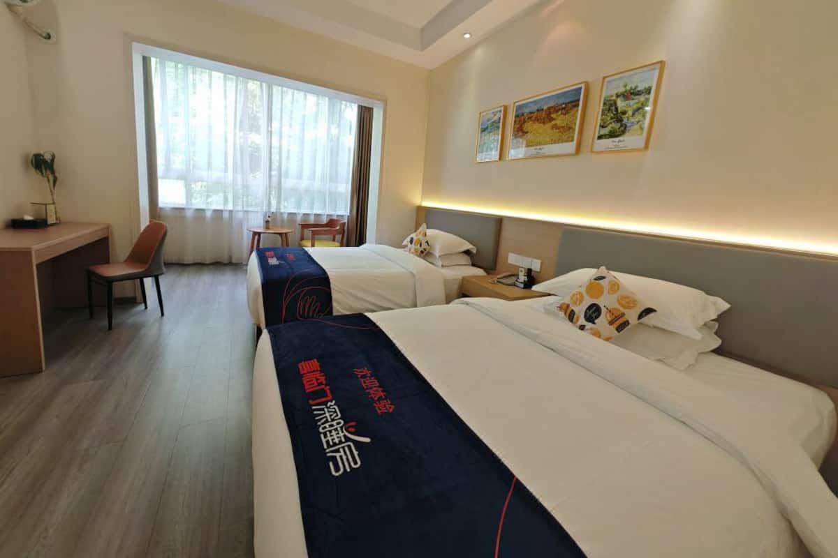 A hotel room with two beds, a desk, a chair, and a large window.
