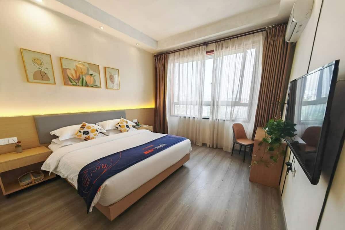 A hotel room with a large bed, a desk, a chair, a TV, and a window with curtains.