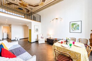 Un vaste espace de vie doté d’un haut plafond, une table à manger pour quatre personnes et un escalier menant à un niveau supérieur.