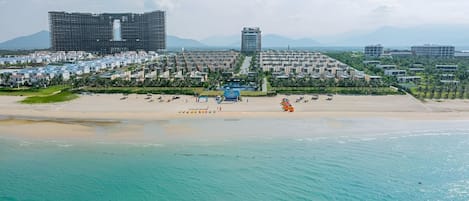 A coastal hotel with a beach, a pool, and modern buildings in the background.