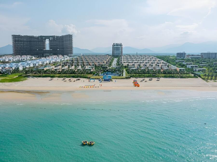 A coastal hotel with a beach, a pool, and modern buildings in the background.