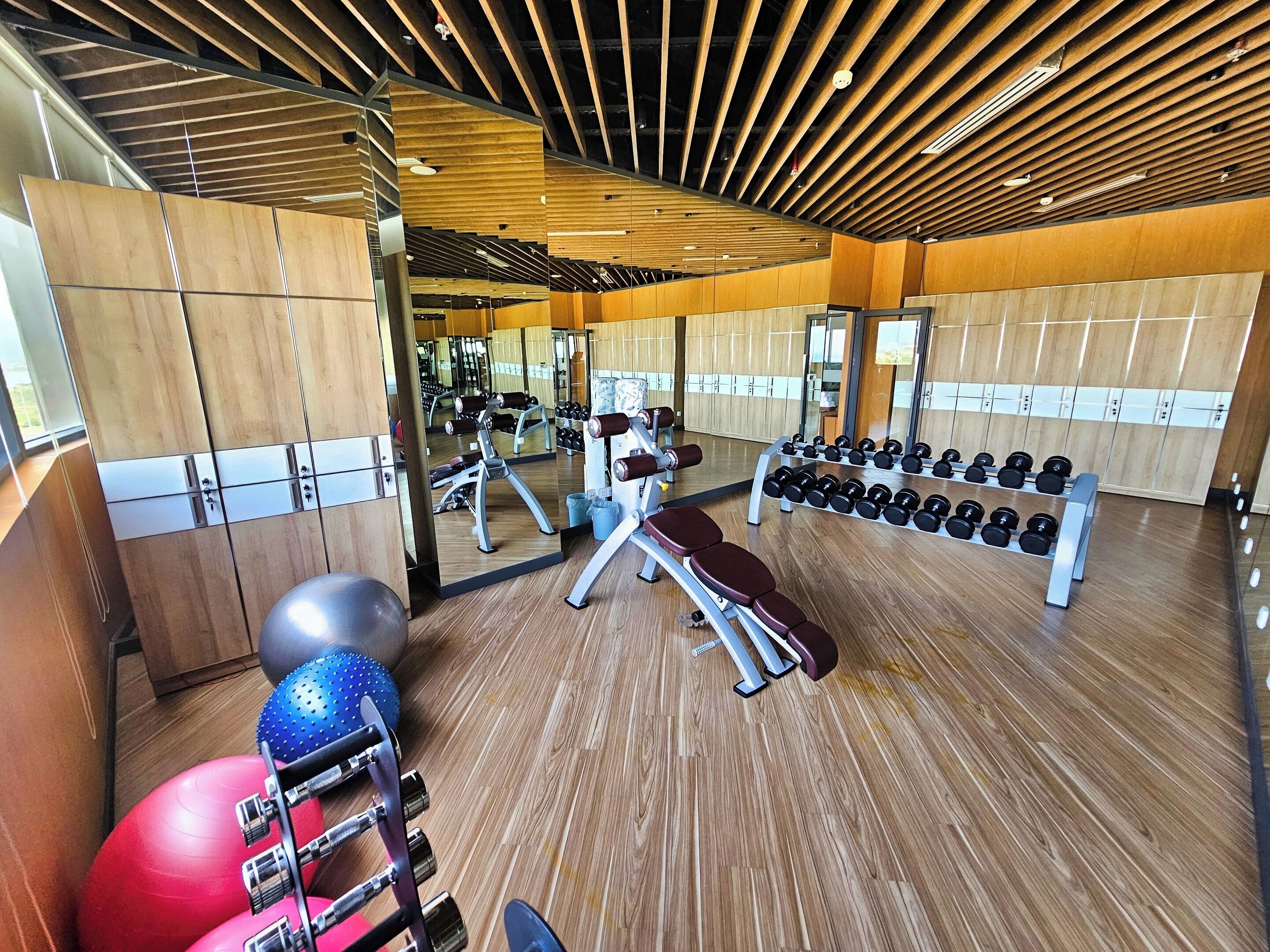 A gym with wooden floors, exercise equipment, and lockers.