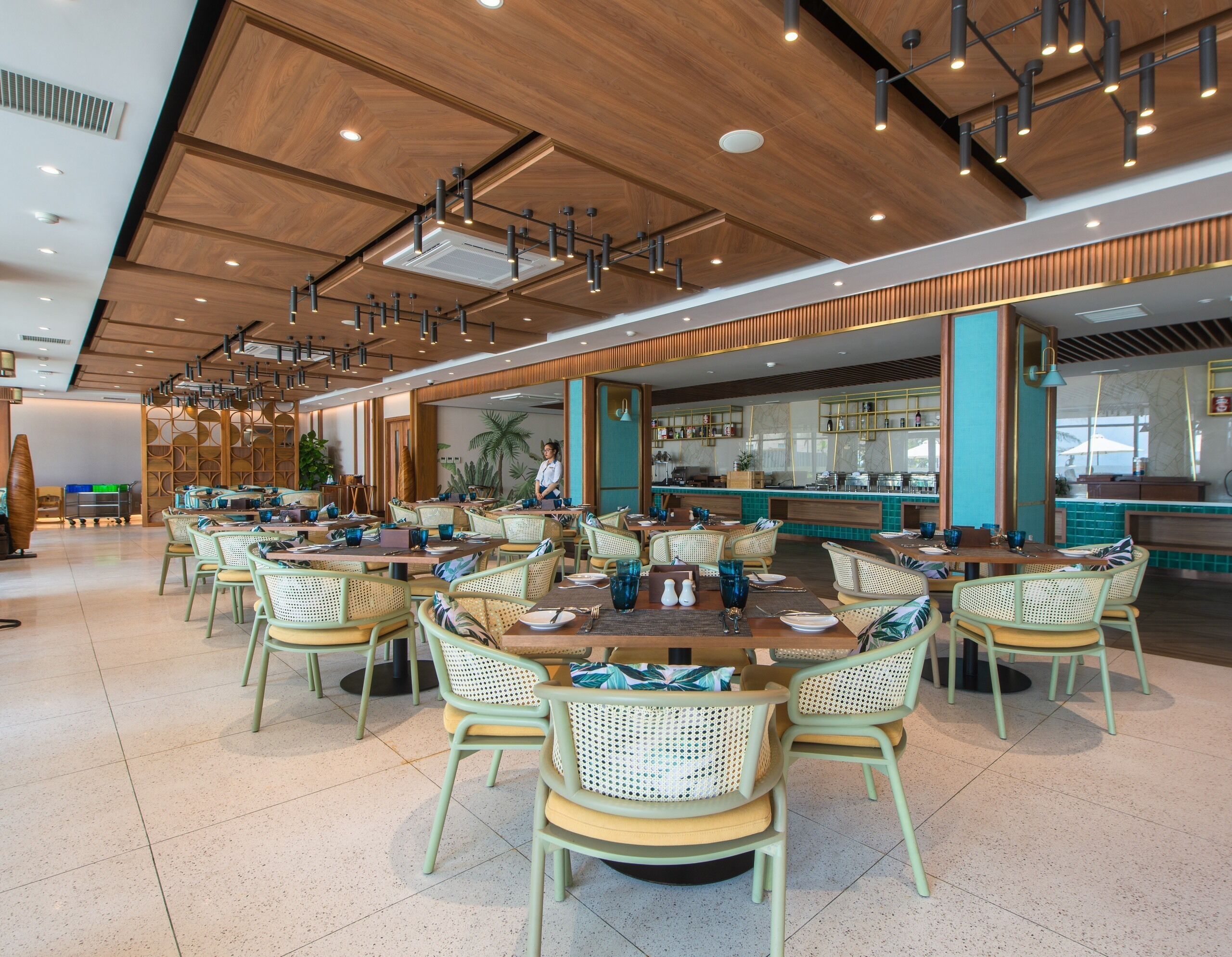 A spacious restaurant with high ceilings, wooden paneling, and a variety of seating arrangements including round tables and wicker chairs.