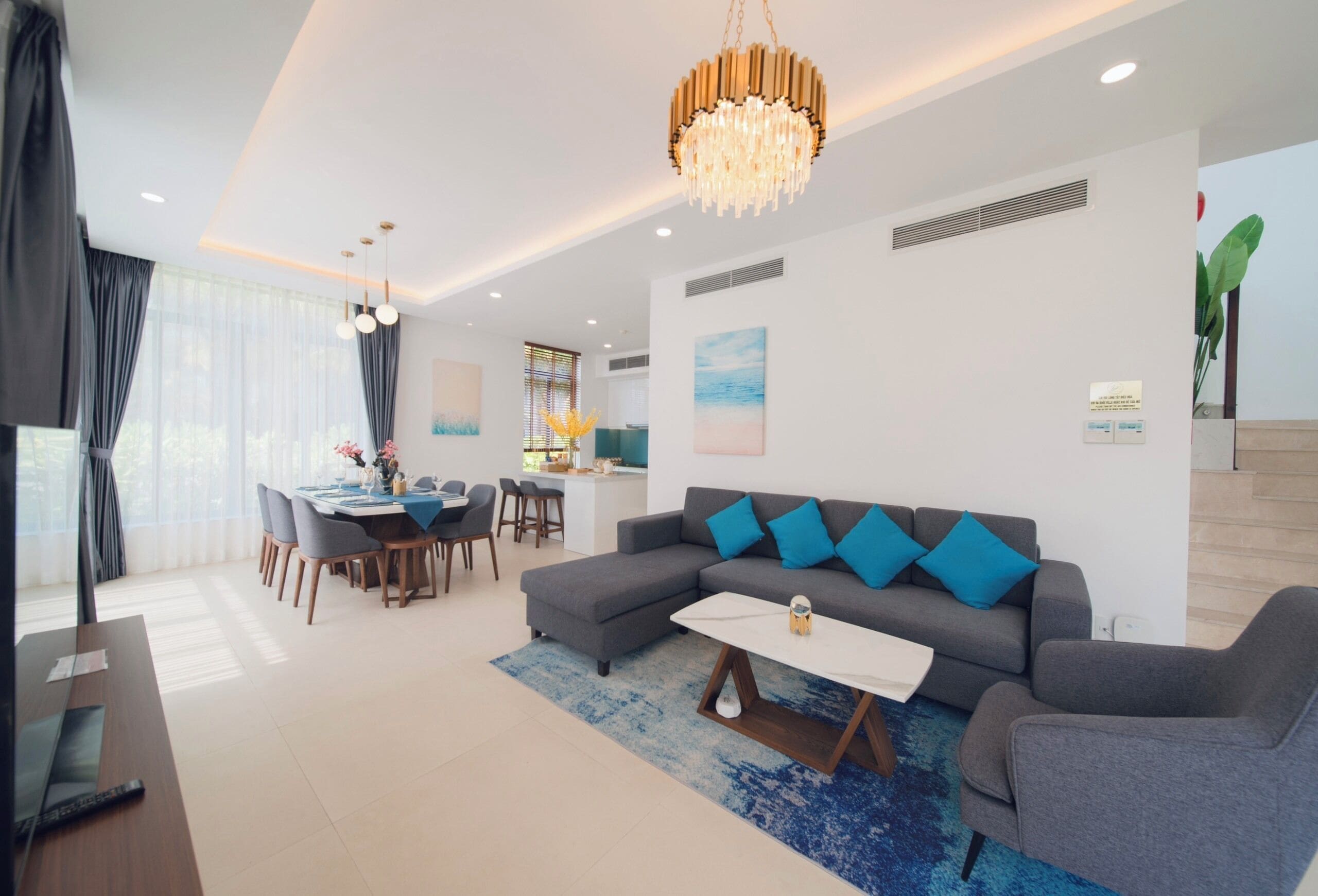 Ein modernes Wohnzimmer mit einem grauen Sofa, blauen Kissen, einem Couchtisch und einer Chandelier.
