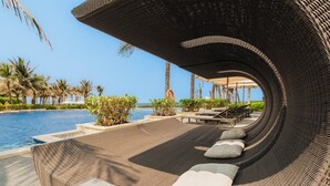 A curved lounge area with wicker furniture and cushions, overlooking a swimming pool and palm trees. - Hese Pool Villas & Resort Cam Ranh (Cam Lam)