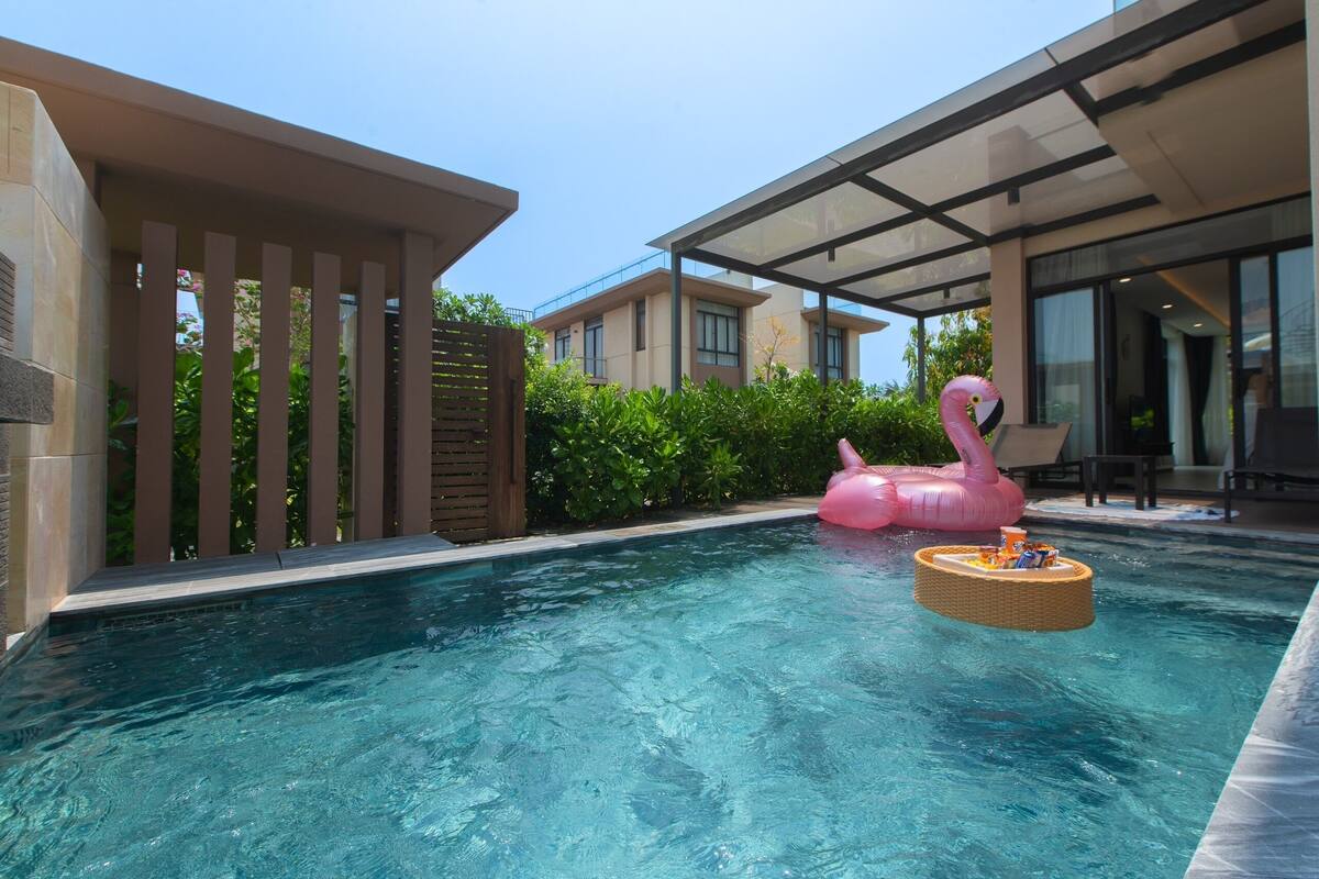 A swimming pool with a pink flamingo float and a wicker lounge chair.